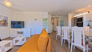 A modern living room with a sofa, TV, white furniture, and a dining area with chairs and a table. - Villa Mambo (Zupa dubrovacka)