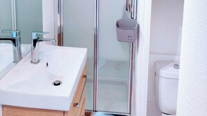 Ein modernes Badezimmer mit einer gläsernen Duschkabine, einem weißen Waschbecken mit Holzschrank und einer Toilette.