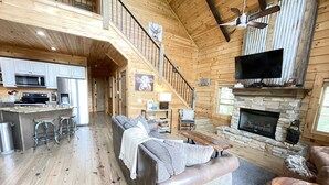 A spacious living area with a wooden interior, a fireplace, a sofa, and a television mounted on the wall.