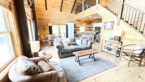 A spacious log cabin interior with a living area, kitchen, and a staircase leading to an upper level.