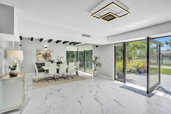 A modern interior with a dining area, large windows, and a view of greenery.