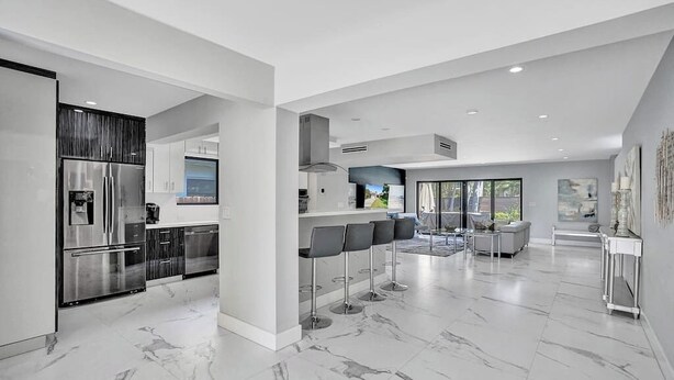 A modern kitchen with a stainless steel refrigerator, a bar area with stools, and a dining space with a sofa and table. - Welcome to Paradise! 1 mile to beach heated pool! (Hollywood)