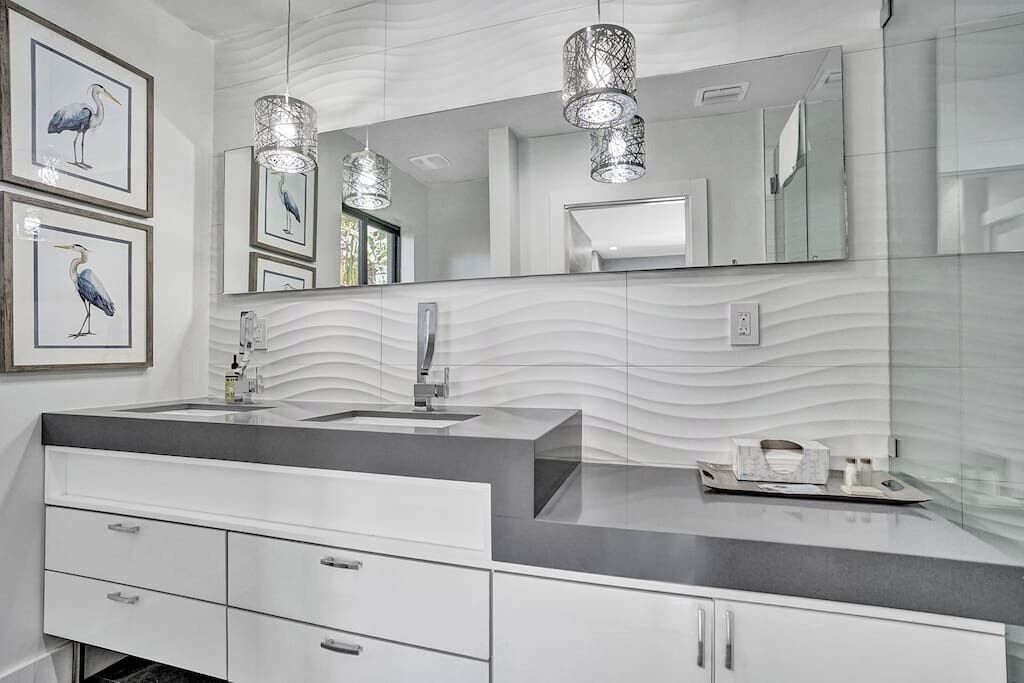 Un baño moderno con un espejo grande, dos lámparas colgantes y una obra de arte enmarcada en la pared.