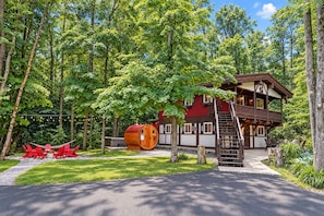 A two-story lodge with a wooden exterior, a large barrel-shaped structure, and a red chair set. - Chalet Getaway: Hot Tub, Sauna & Fire Pit (Bellaire)