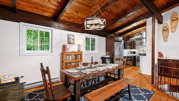 Un comedor con una mesa de madera dispuesta para seis personas, rodeada de sillas, un banco y una estantería.