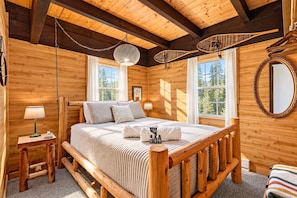 A wooden cabin bedroom with a bed, bedside tables, and a large window. - Chalet Getaway: Hot Tub, Sauna & Fire Pit (Bellaire)