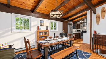 Un coin repas avec une table en bois dressée pour six personnes, un banc et une bibliothèque.
