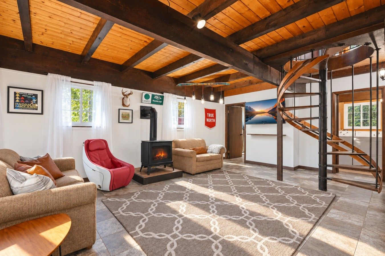 A cozy living room with a fireplace, a red chair, a sofa, and a spiral staircase.