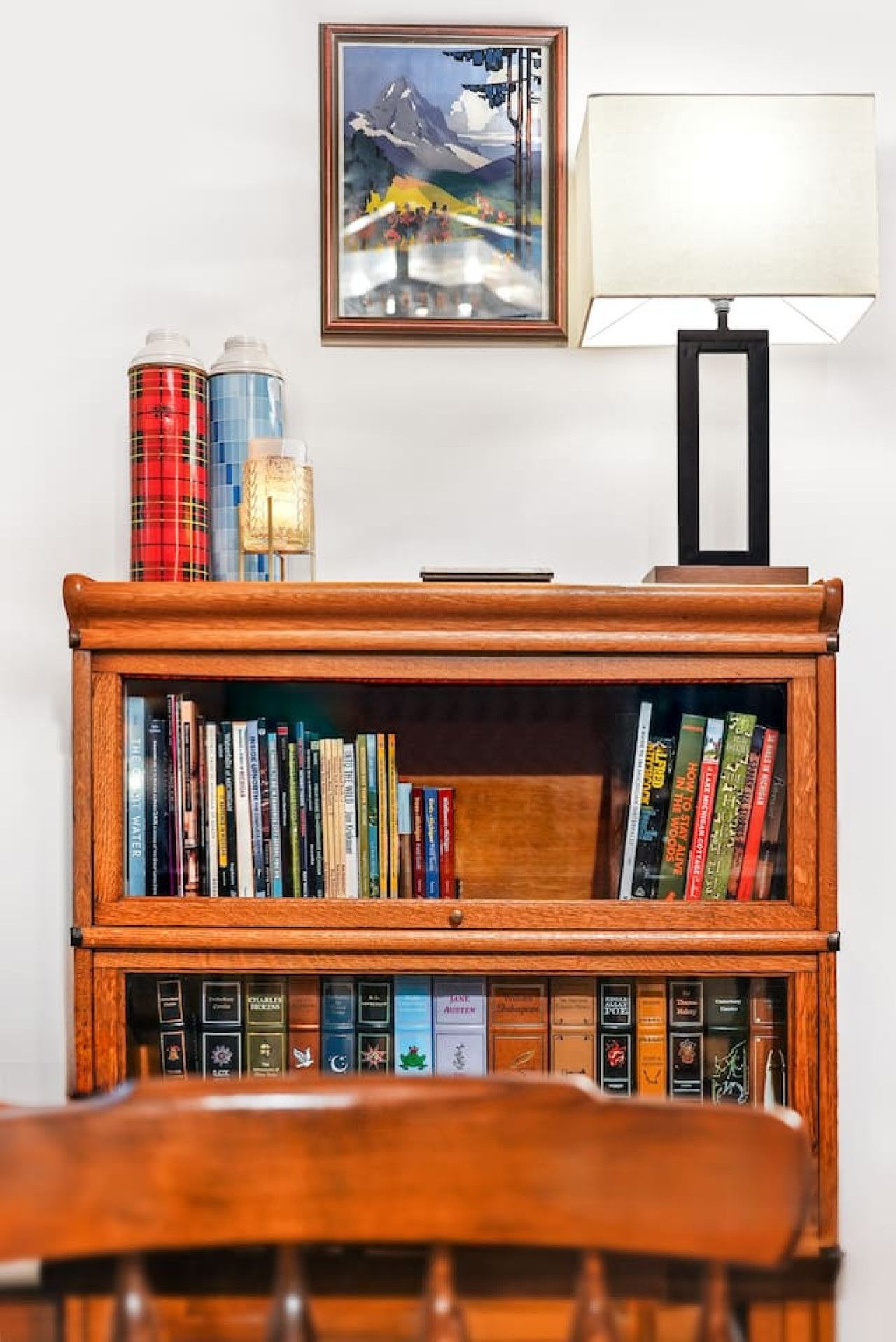 Een houten boekenkast met boeken en decoratieve objecten, een ingelijst schilderij en een tafellamp.