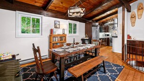 A dining area with a wooden table set for six, surrounded by chairs, a bench, and a bookshelf. - Chalet Getaway | Hot tub | Sauna | Firepit | Pool (Bellaire)