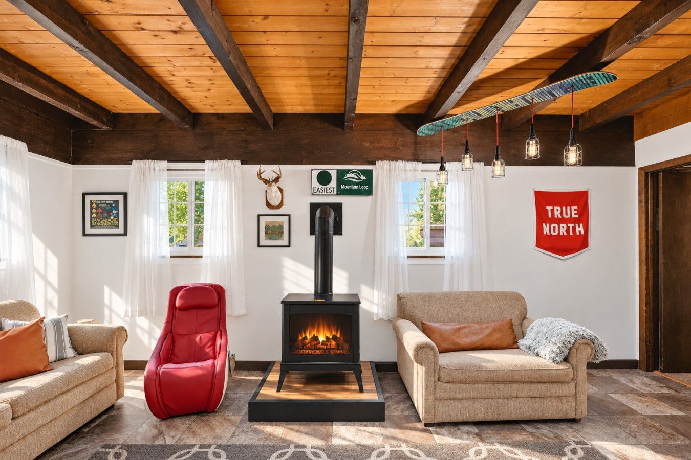 A cozy living room with a fireplace, two sofas, a red chair, and a 'TRUE NORTH' sign.