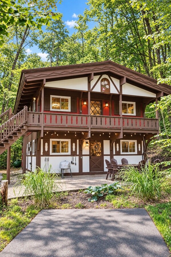Un bâtiment de style chalet doté d’un balcon, d’un escalier et d’un coin repas avec des sièges à l’extérieur.