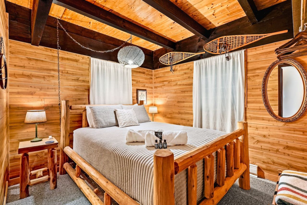 A wooden cabin-style bedroom with a bed, bedside table, lamp, and a hanging light fixture.