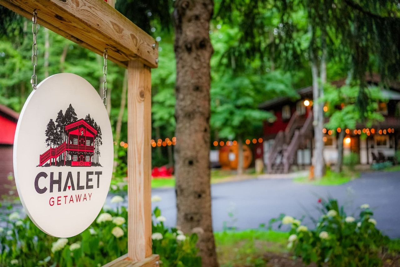 A sign for "CHALET GETAWAY" with a red chalet illustration, hanging on a wooden post.