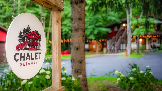 A sign for "CHALET GETAWAY" with a red chalet illustration, hanging on a wooden post. - Chalet Getaway | Hot tub | Sauna | Firepit (Bellaire)