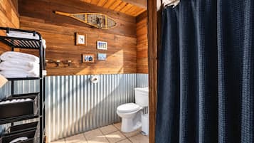 Une petite salle de bain avec un plafond en bois, des toilettes et un rideau de douche.