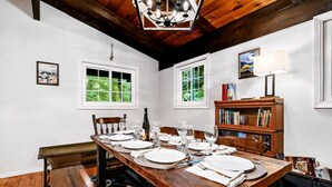 A dining area with a wooden table set for six, white walls, and a bookshelf with books and a lamp. - Chalet Getaway | Hot tub | Sauna | Firepit (Bellaire)