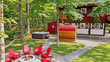 Un bain à remous en forme de tonneau en bois, une chaise Adirondack rouge et un foyer en pierre dans un jardin.