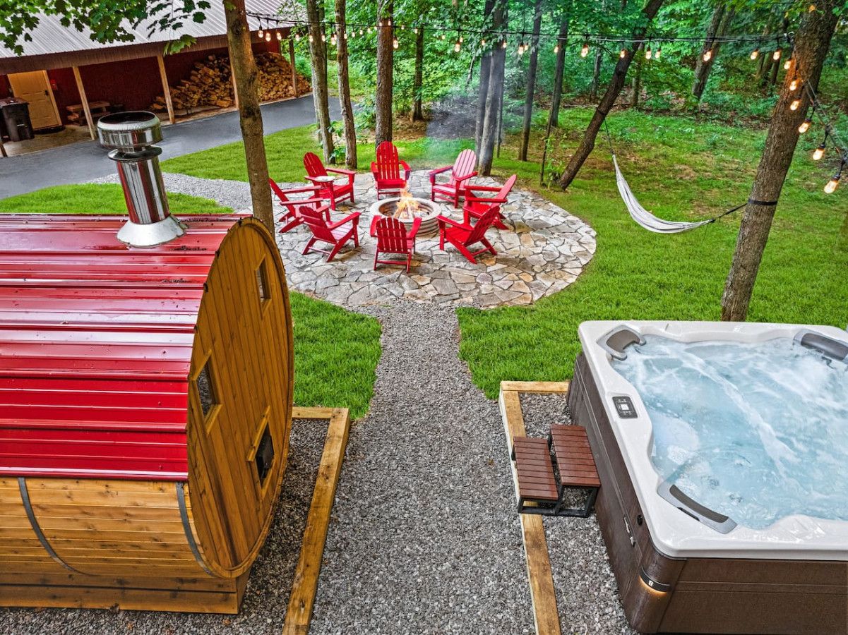 Een jacuzzi, een houten vat, en een vuurkuil met rode Adirondack-stoelen in een tuin.