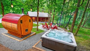 A rustic cabin with a wooden exterior and a red roof, a hot tub, and red Adirondack chairs in a forested area. - Chalet Getaway | Hot tub | Sauna | Firepit | Pool (Bellaire)