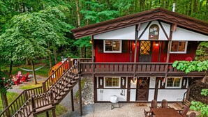 A chalet-style building with a wooden staircase leading to a deck, surrounded by lush greenery. - Chalet Getaway | Hot tub | Sauna | Firepit (Bellaire)