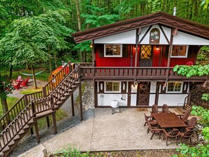A chalet-style building with a wooden staircase leading to a deck, surrounded by lush greenery. - Chalet Getaway | Hot tub | Sauna | Firepit (Bellaire)