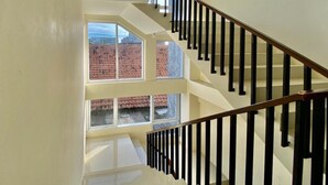 A multi-level interior with a staircase, large windows, and a view of red-roofed buildings outside. - Reddoorz @ Arkana Seturan (Depok)