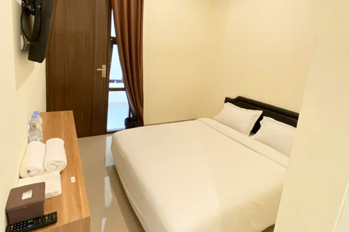 A hotel room with a bed, a wooden desk with a remote control, towels, and a bottle of water.