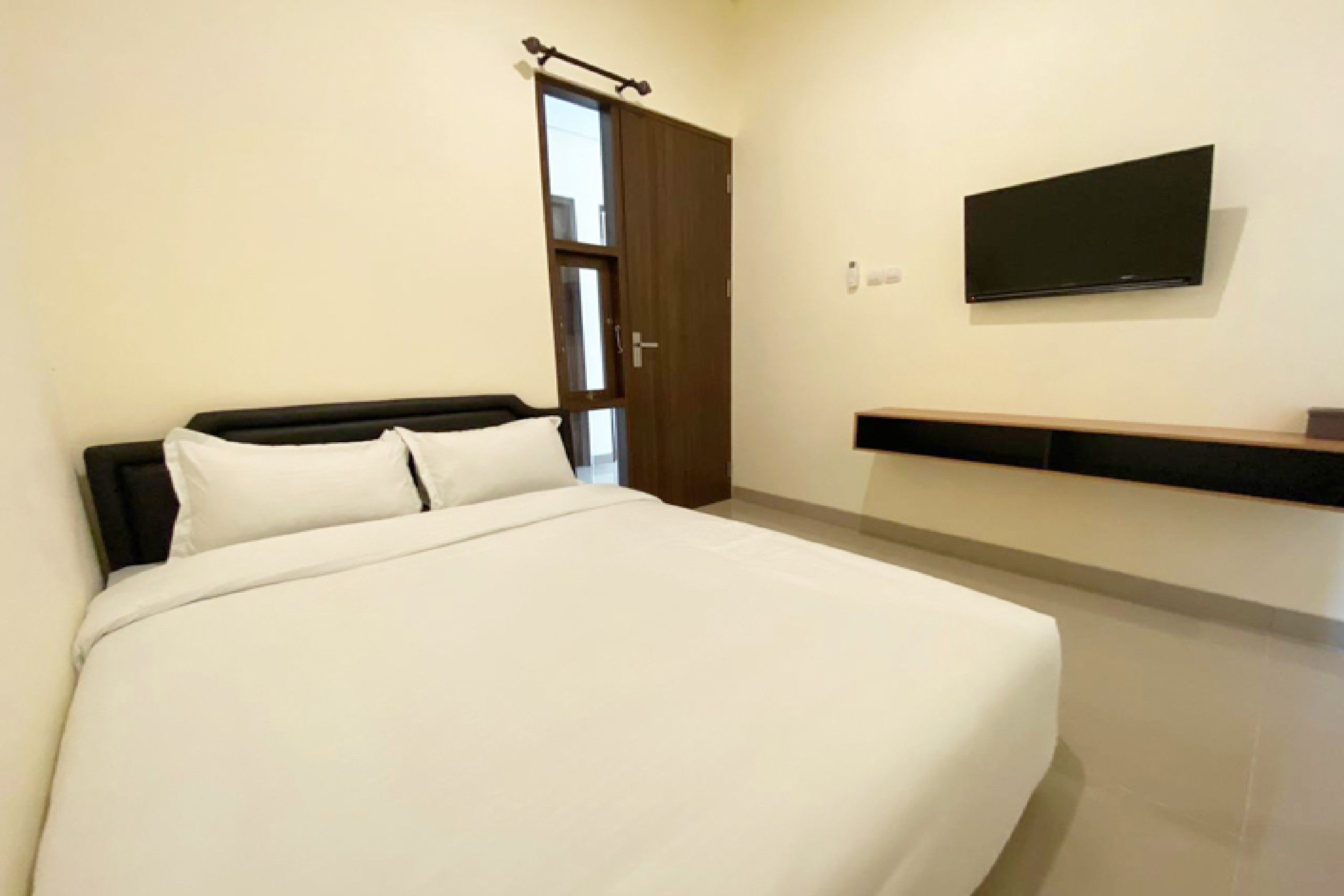 Un dormitorio con cama, una puerta, televisor montado en la pared y una pequeña repisa.