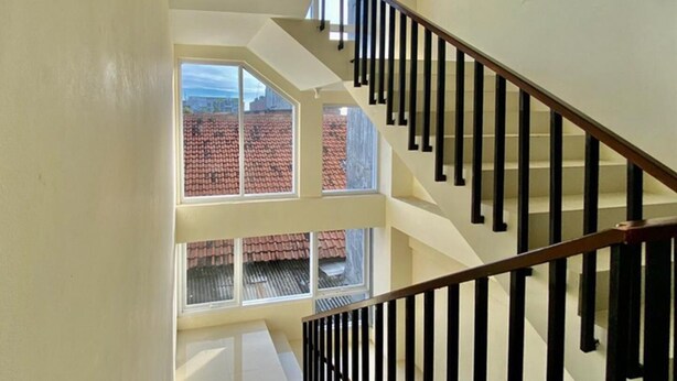 Un interior de varios niveles con una escalera, ventanas amplias y vistas de edificios de tejados rojos al exterior.