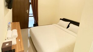 Una habitación de hotel con una cama, un escritorio de madera con un control remoto, una botella de agua y una toalla.