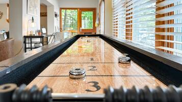 A shuffleboard table with numbered ends, a ceiling fan, and a view of a room with a window and blinds.