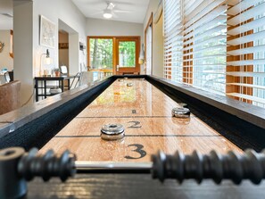 A shuffleboard table with numbered ends, a ceiling fan, and a view of a room with a window and blinds. - Firefly Cottage; Prime Cove location, large dock, grill, screened in porch  (Lake Ozark)