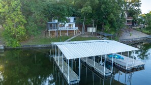 A dock with a covered area, a house with a balcony, and a small boat. - Firefly Cottage; Prime Cove location, large dock, grill, screened in porch  (Lake Ozark)