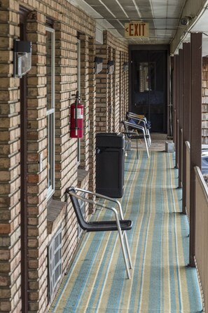Un couloir avec un tapis à rayures, des chaises en métal, un extincteur et un panneau indiquant la sortie.