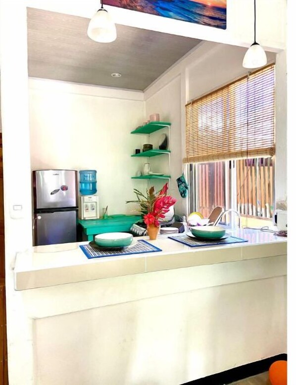 A kitchen with a refrigerator, shelves, and a window with blinds.