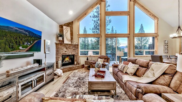 A spacious living room with a large fireplace, comfortable seating, and a scenic view through large windows.