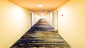 A long, narrow hotel corridor with a carpeted floor and light-colored walls.