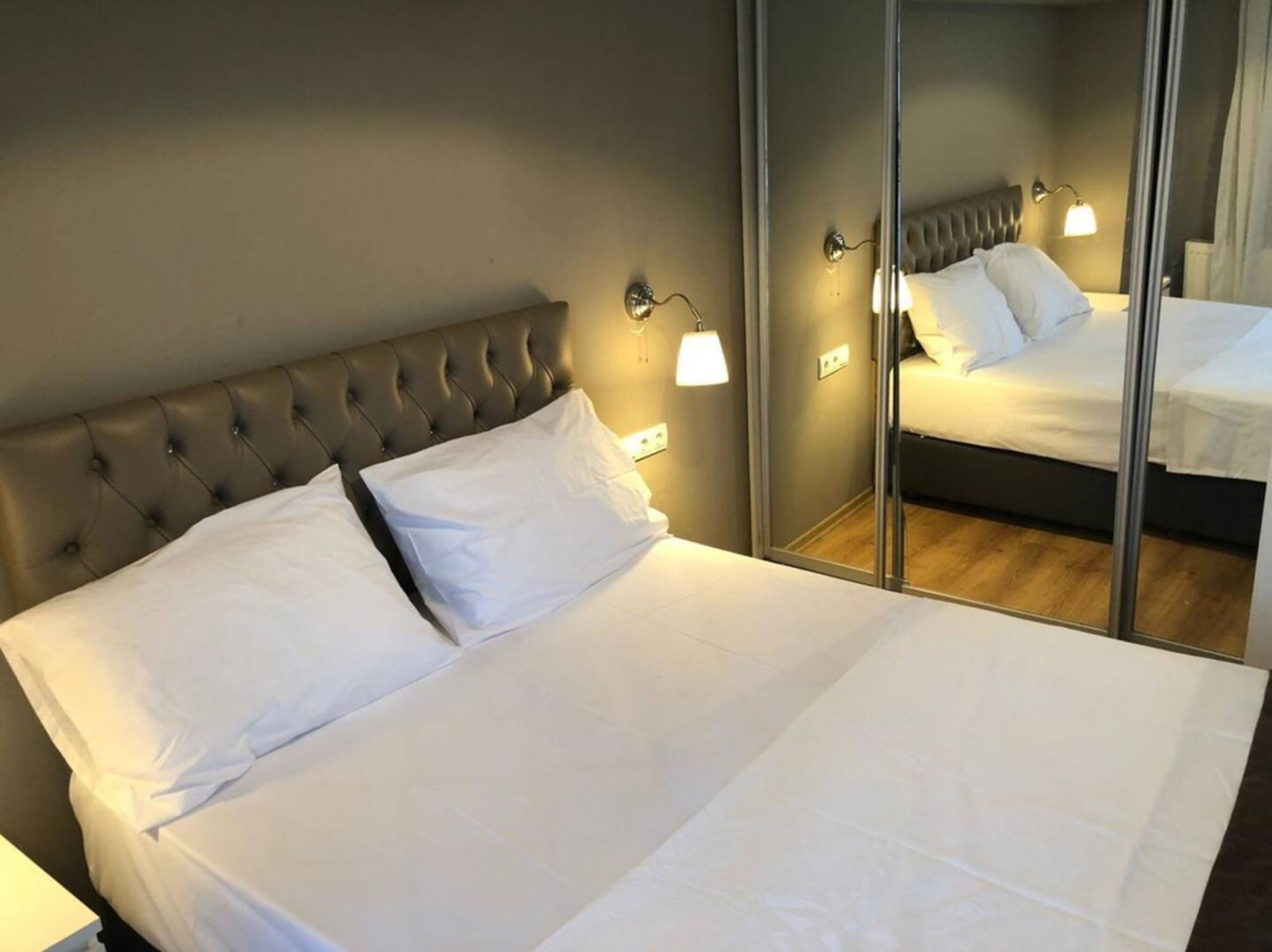 A neatly made bed with white linens, a tufted headboard, and bedside lamps.