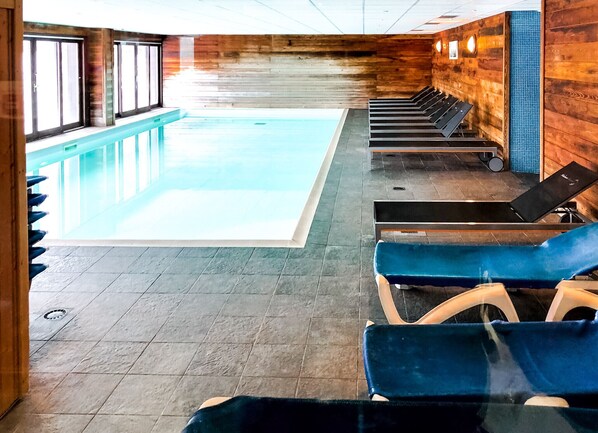 Une piscine avec un sol carrelé et un mur en bois. On y trouve des chaises longues et un escalier menant à un niveau supérieur.