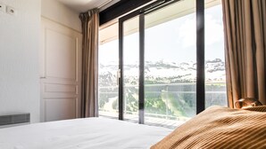 Ein Hotelzimmer mit einem großen Bett, Blick auf eine gebirgige Landschaft durch eine Schiebetür und einem Vorhangfenster.