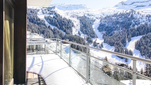 Ein Balkon mit Glasgeländer mit Blick auf eine verschneite Berglandschaft.