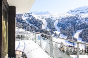 Un balcon doté d’une balustrade en verre, offrant une vue sur un paysage montagneux enneigé.