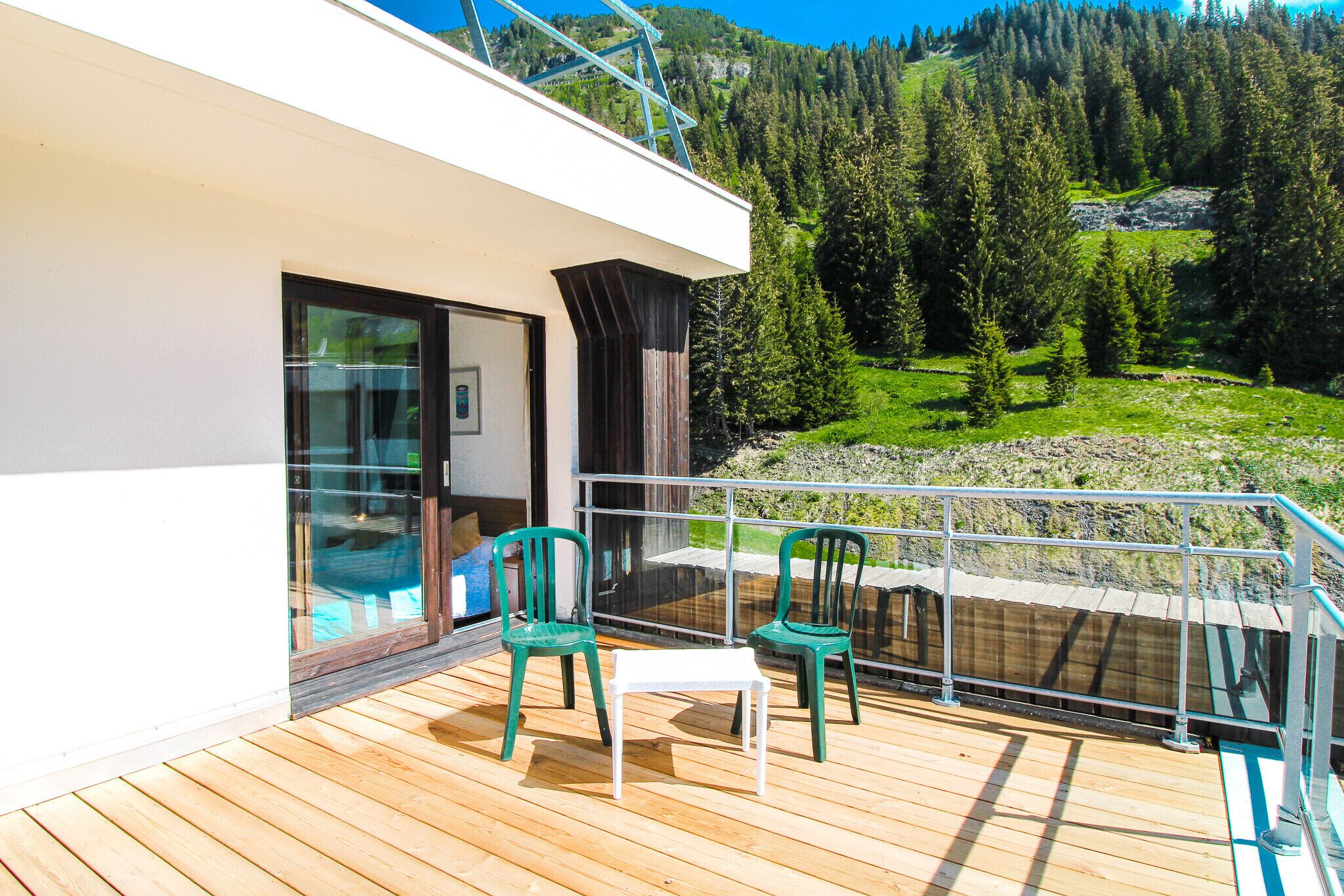 A balcony with wooden flooring, two green chairs, and a white table.