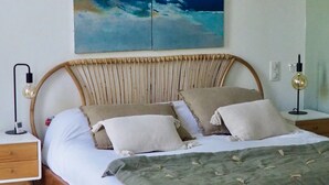 Un dormitorio con cama de madera, ropa de cama blanca, una manta verde y un cuadro abstracto grande en la pared.