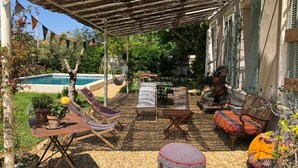 Un área de estar al aire libre con techo, con una piscina al fondo, una mesa con planta en maceta y diferentes opciones de asientos.