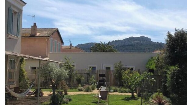 Una piscina con agua cristalina azul, rodeada por un jardín con diversas plantas y una cerca de madera.