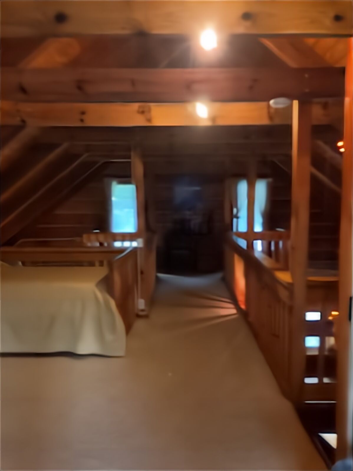 A narrow, wooden interior hallway with a bed on the left and a staircase on the right.