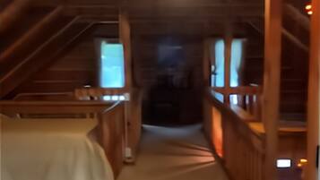 A narrow, wooden interior hallway with a bed on the left and a staircase on the right.