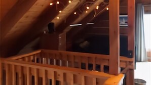 An attic room with wooden beams, a wooden railing, and string lights.